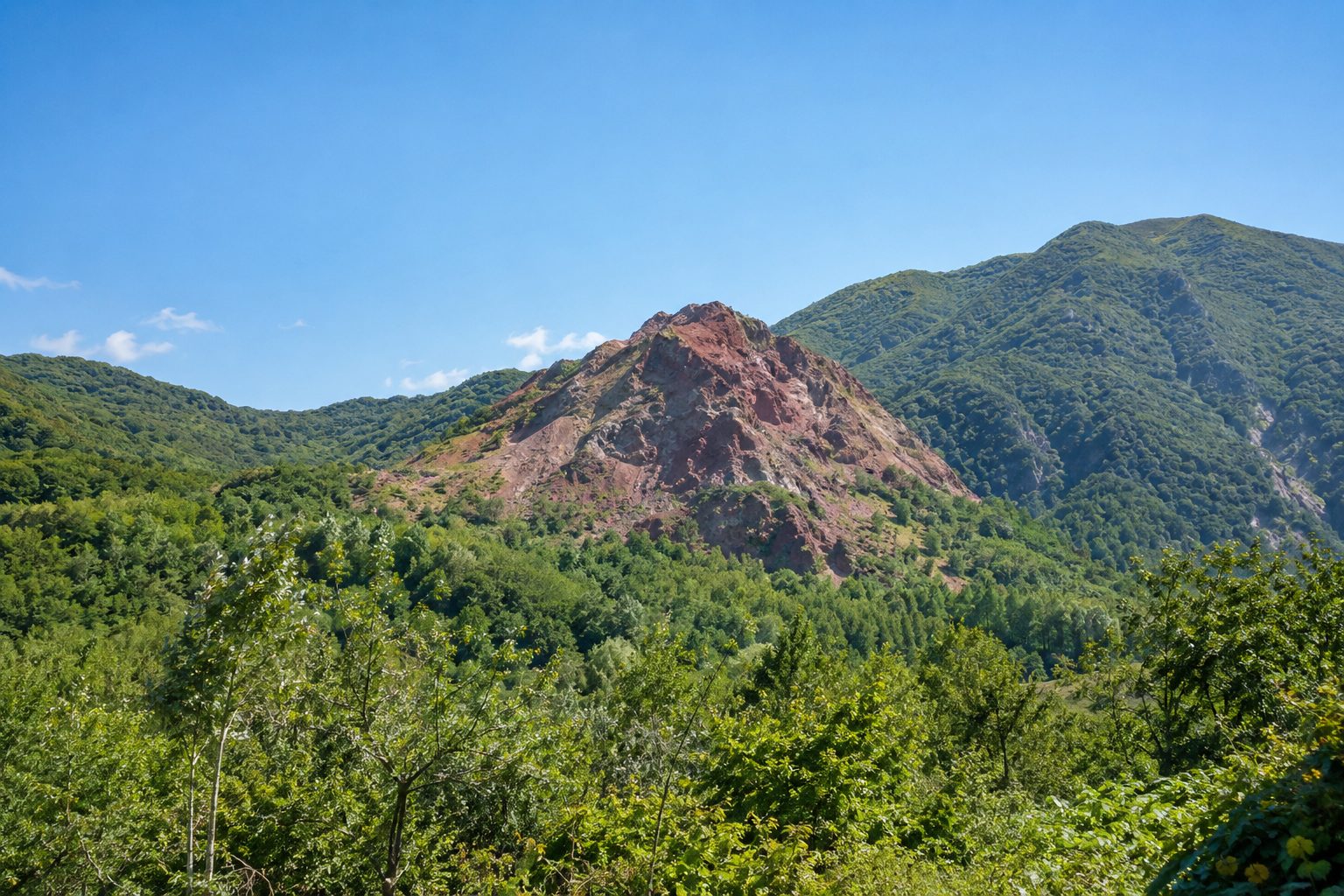 赤茶色の岩肌の火山と緑の山