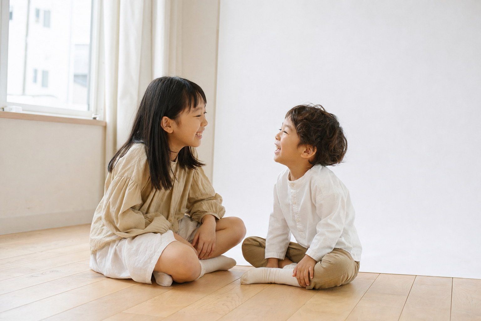 木の床で向かい合って笑う姉と弟（掲載イメージ）