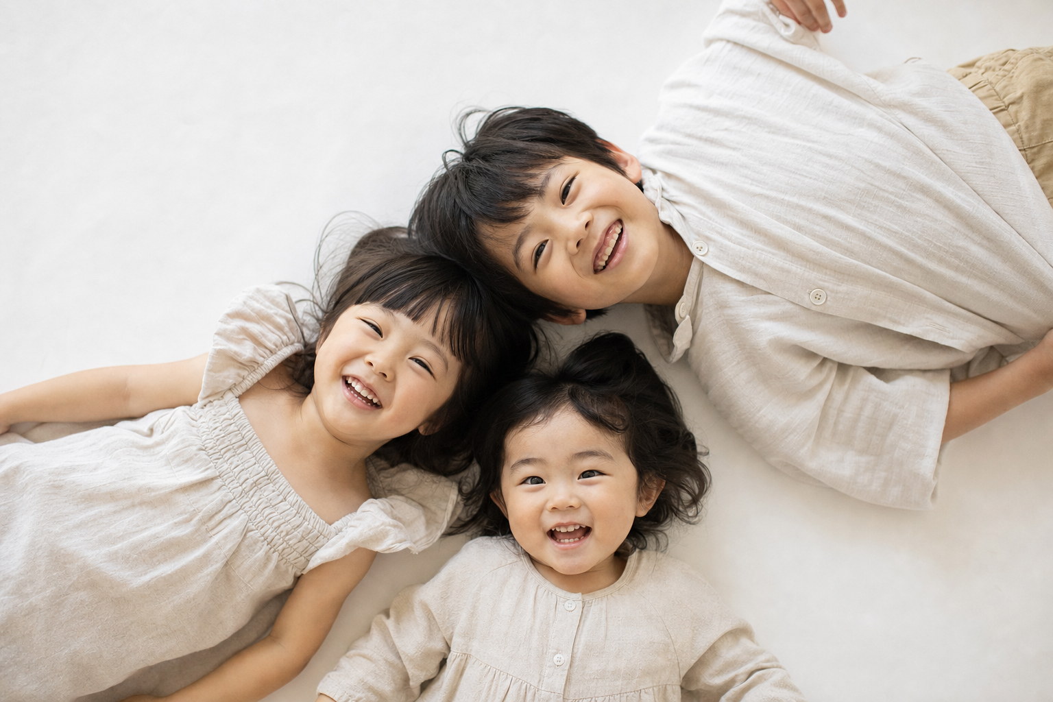 背景紙の上で頭を寄せ合って寝転ぶ三人きょうだい（掲載イメージ）