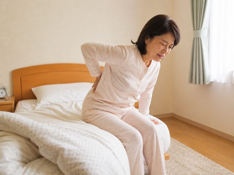 朝、起き上がるときに腰をかばう女性